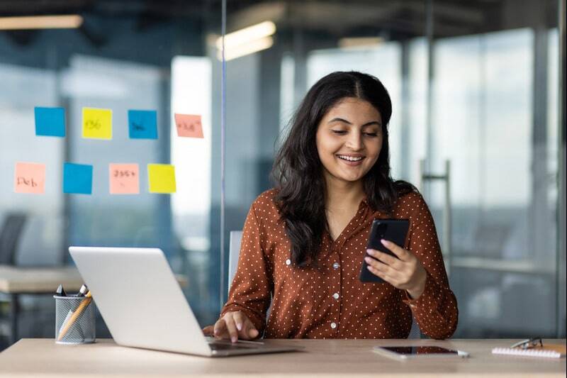 A female job candidate on their phone and laptop at the same time, rapidly submitting applications to different companies.